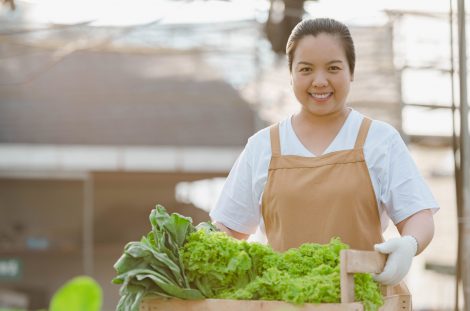 Portrait of Asian farmer woman holding wooden box full of fresh raw vegetables. Organic farm concept.